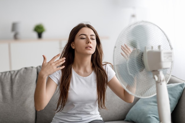 Foto triste joven europea sufre de un clima insoportablemente demasiado caliente atrapa el aire frío del ventilador en la vida