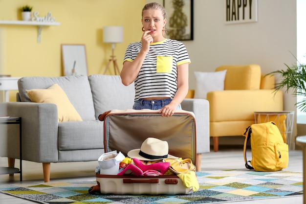 Triste joven y maleta con muchas cosas en casa. Concepto de viaje