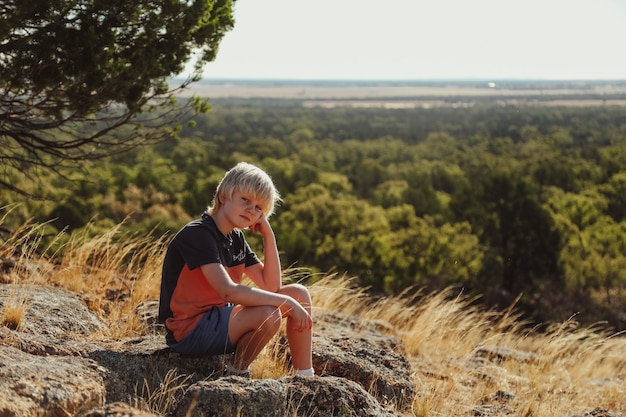 Triste joven sentado sobre una roca en un paisaje rural