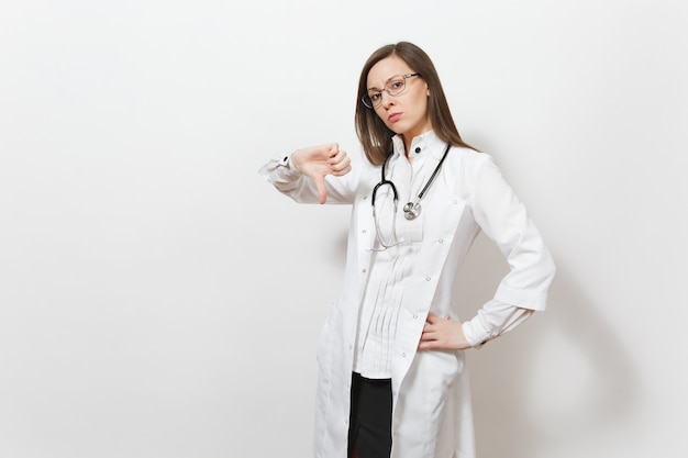 Triste malestar hermosa joven médico con estetoscopio, gafas aisladas sobre fondo blanco. Doctora en bata médica muestra los pulgares hacia abajo gesto. El personal sanitario, la salud, el concepto de medicina.