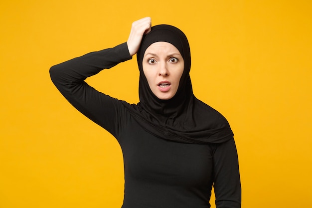 Triste, malestar, llanto, confundido, joven, árabe, musulmán, en, hijab, ropa negra, posar, aislado, en, amarillo, pared, portrait. Concepto de estilo de vida religioso del Islam de la gente.