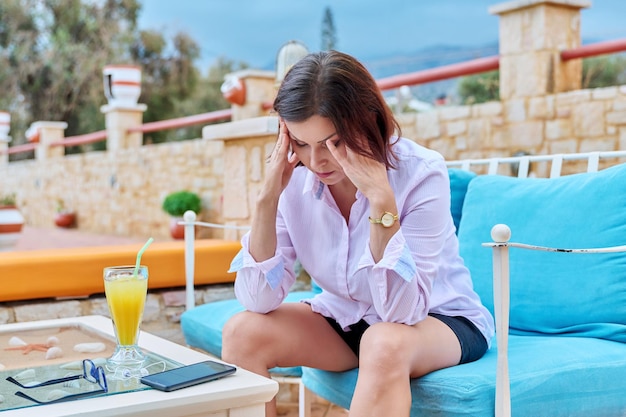 Triste malestar mujer madura sentada al aire libre en la mesa de café con smartphone