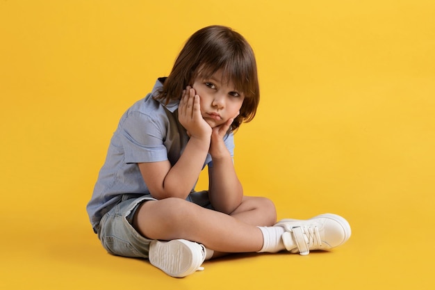 Triste menino infeliz sentado no chão e sofrendo sozinho, apoiando o queixo nas mãos, olhando para o espaço livre da câmera