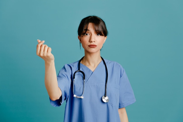 Triste mostrando dicas gesticulam jovem médica usando estetoscópio uniforme de quinto isolado em fundo azul