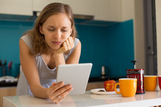 Triste mujer bonita con tableta en cocina