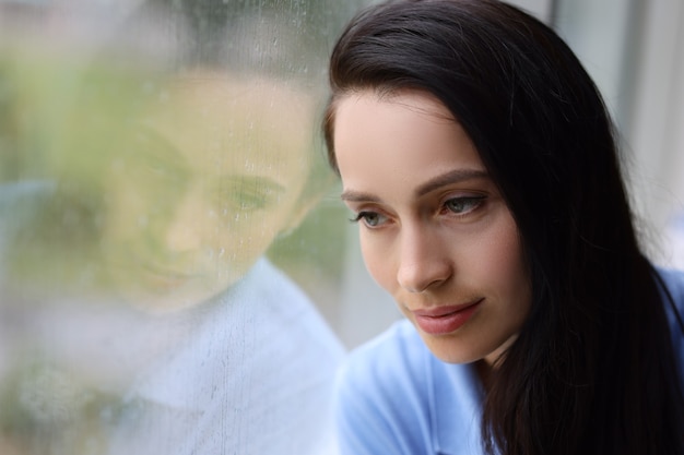 Triste mujer cansada mira por la ventana mientras llueve concepto de depresión de otoño