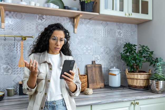 Triste mujer hispana en depresión leyendo malas noticias en un teléfono inteligente mujer con gafas y cabello rizado