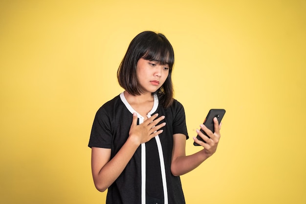 Triste mujer joven asiática mientras usa el teléfono móvil en un fondo aislado