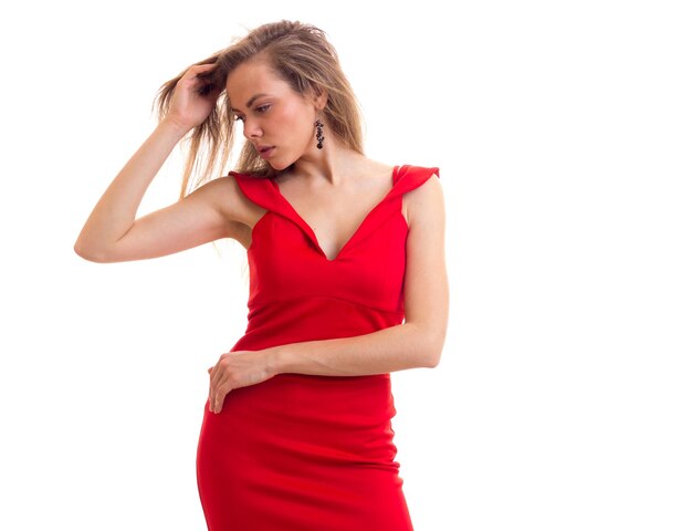 Triste mujer joven con cabello castaño largo en diminuto vestido rojo con aretes negros en estudio