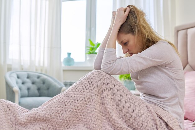 Triste mujer de mediana edad estresante sentada en casa en la cama bajo una manta