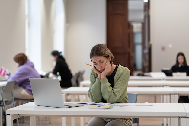 Triste mujer de mediana edad estudiante madura en la biblioteca sintiéndose cansada y aburrida en la clase en línea