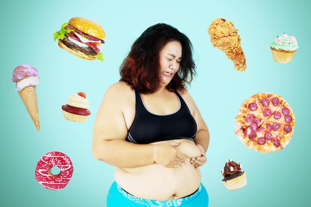 Triste mujer obesa pellizcando su grasa del vientre en el estudio