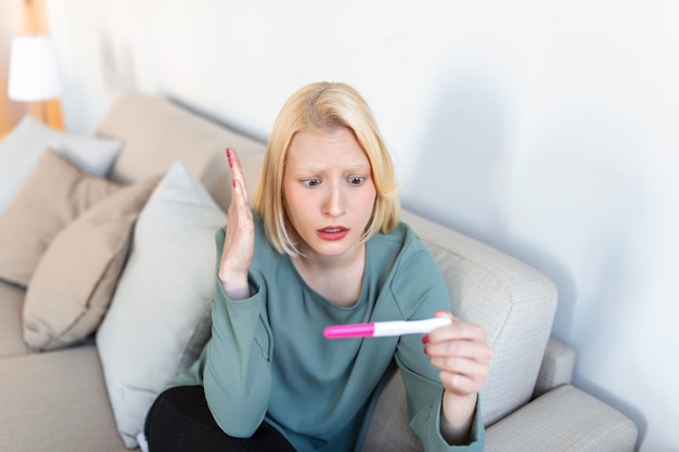 Triste mujer preocupada revisando su reciente prueba de embarazo sentada en el sofá en casa Maternidad parto y problemas familiares concepto embarazo no deseado