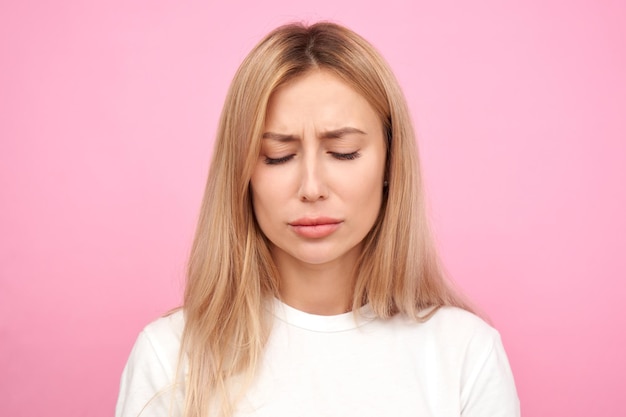 Triste mujer rubia en depresión siente dolor mental disgustado cara aislado sobre fondo de color rosa