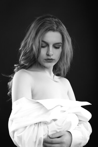 Triste mujer sensual viste camisa de hombre posando en las sombras en el estudio. Imagen en blanco y negro