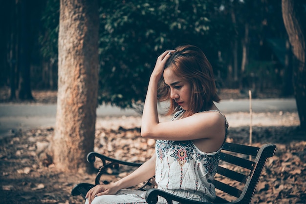 Triste mujer sentada en el banco en el parque estilo vintagePasó la historia mucho peorconcepto de angustia de la gente de Tailandia