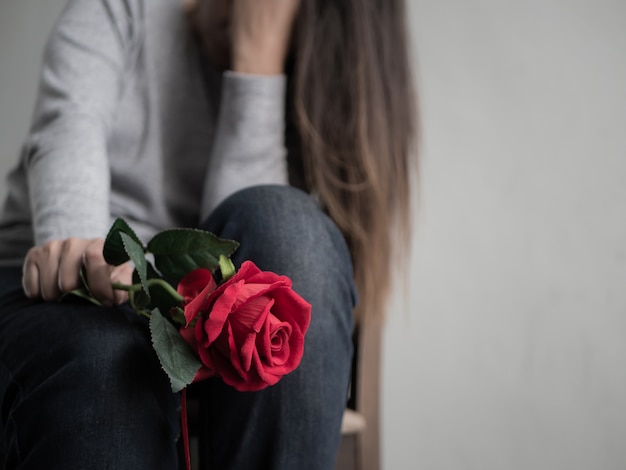 Triste mujer sentada y llorando con rosa roja en la mano