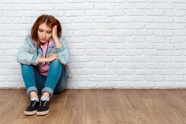 Triste mujer sentada en el piso cerca de la pared