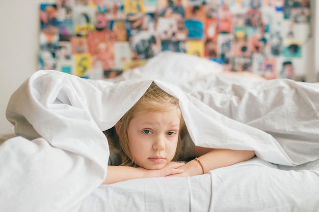 Triste niña acostada debajo de una manta blanca