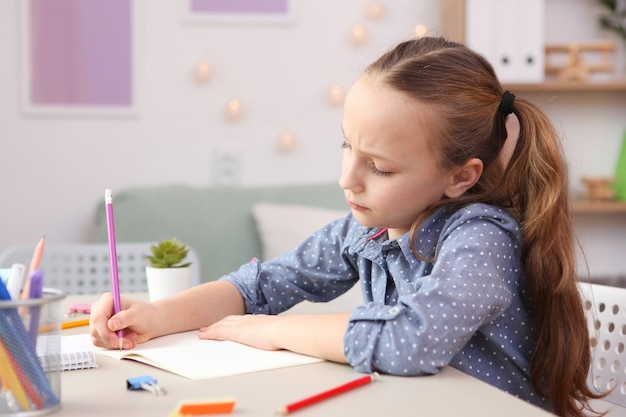 Triste niña cansada hace la tarea en el interior de la habitación