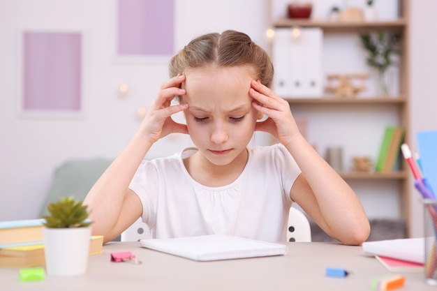 Triste niña cansada hace la tarea en el interior de la habitación