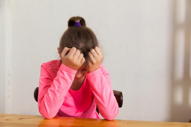 Triste niña preadolescente en suéter rosa en la mesa con expresión triste en su rostro