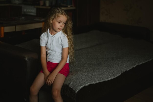 Triste niña preescolar sentada en un sofá en casa