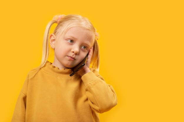 Triste niña rubia hablando por un teléfono móvil sobre un fondo amarillo Closeup retrato