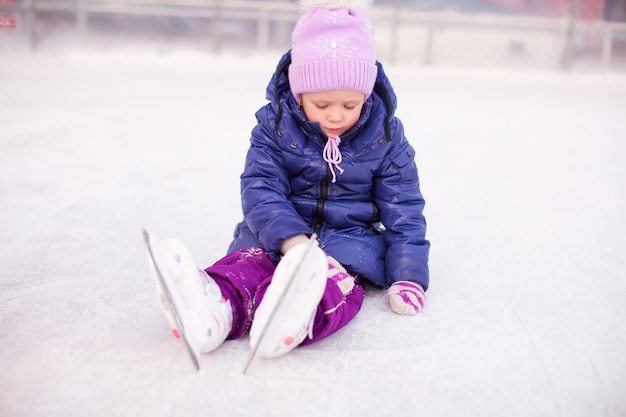 Triste niña sentada en una pista de patinaje después de la caída