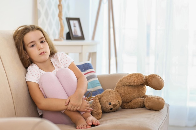 Triste niña sentada en el sofá en la habitación