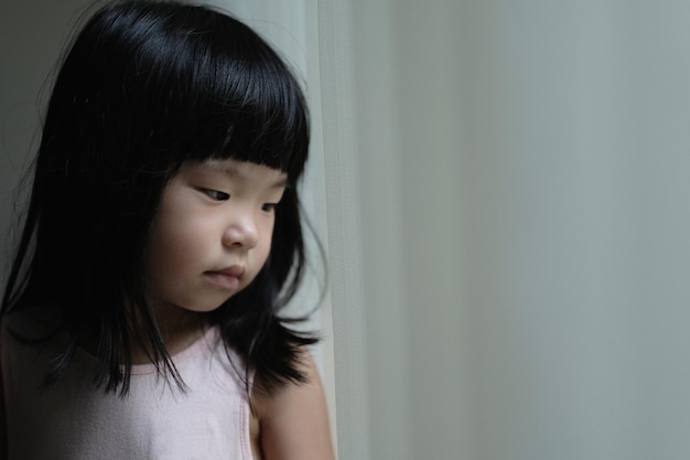 Triste niña solitaria de pie junto a una ventana