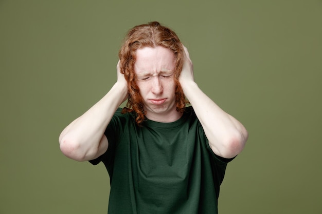 Triste con los ojos cerrados agarró la cabeza joven guapo con camiseta verde aislado sobre fondo verde