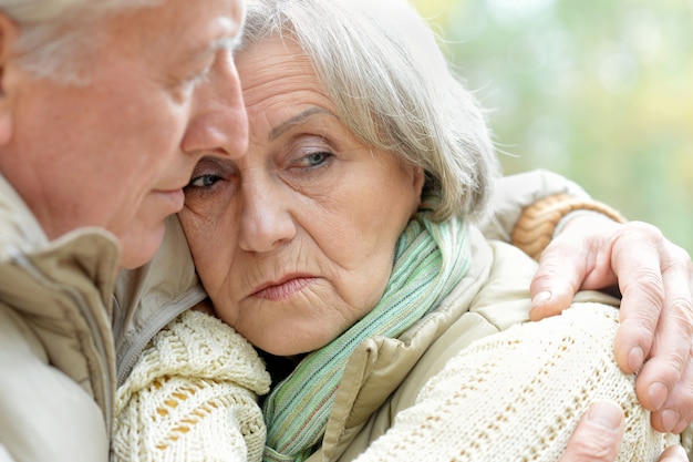 Triste pareja senior de pie en el parque otoño