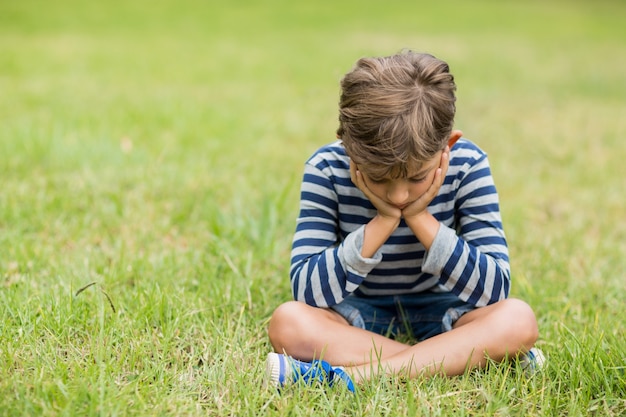 Triste rapaz sentado na grama