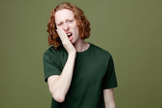 Triste rostro cubierto con la mano joven guapo con camiseta verde aislado sobre fondo verde