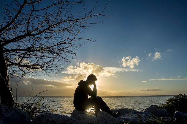 Triste silueta de hombre joven preocupada por la piedra al atardecer, concepto de silueta