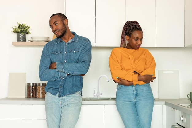 Tristes cónyuges afroamericanos parados uno cerca del otro en la cocina ofendidos después de una pelea en casa