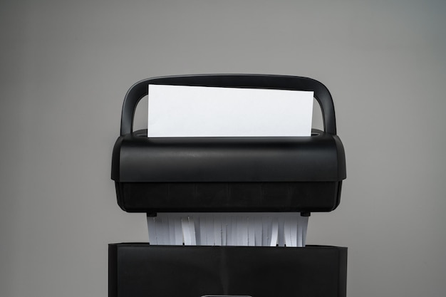 Trituradora de papel negra para cortar papel sobre un fondo gris