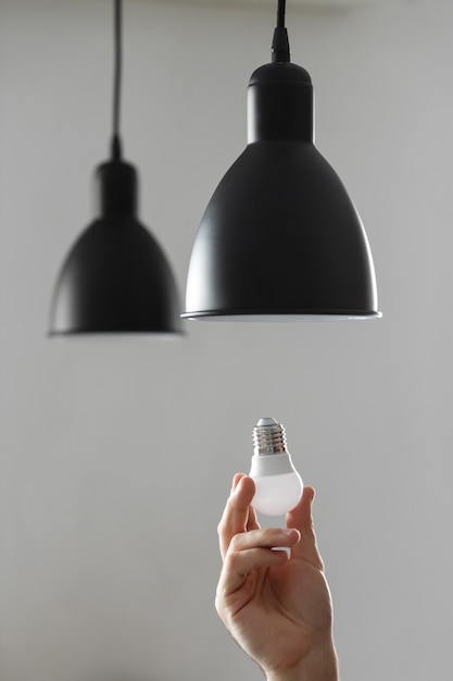 Foto troca da lâmpada por lâmpada led no abajur na cor preta. sobre fundo cinza claro.