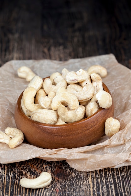 Trockene Cashewnüsse auf einem alten Holztisch und in einer Holzschale, einen Haufen Cashewnüsse auf dem Tisch und in einem Holzteller beim Essen