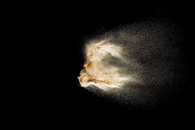 Trockene Flusssandexplosion. Goldenes farbiges Sandspritzen gegen schwarzen Hintergrund.