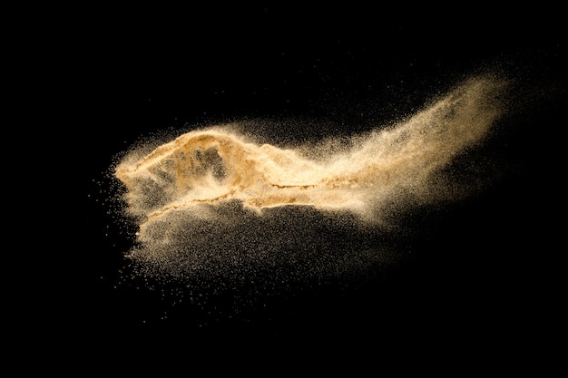 Trockene Flusssandexplosion lokalisiert auf schwarzem Hintergrund. Abstrakte Sandwolke. Braunes farbiges Sandspritzen gegen dunklen Hintergrund.