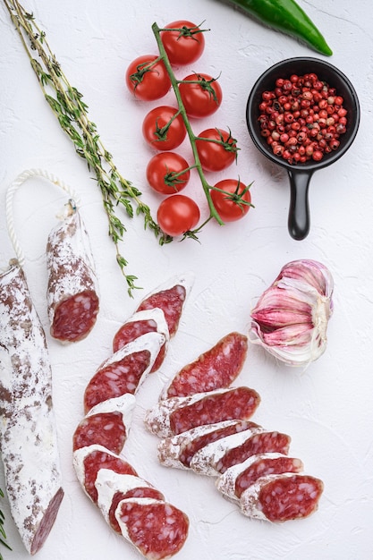 Trockene gehärtete Fuet Salami-Wurstscheiben mit Kräutern auf weißer Oberfläche, Draufsicht.