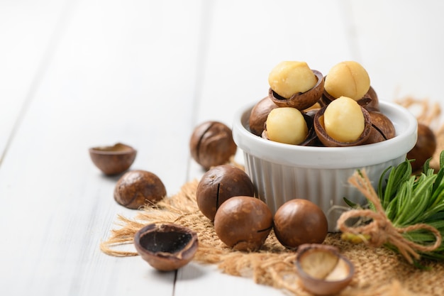 Trockene geröstete Macadamia-Nuss in der weißen Tasse auf weißem Holzhintergrund,