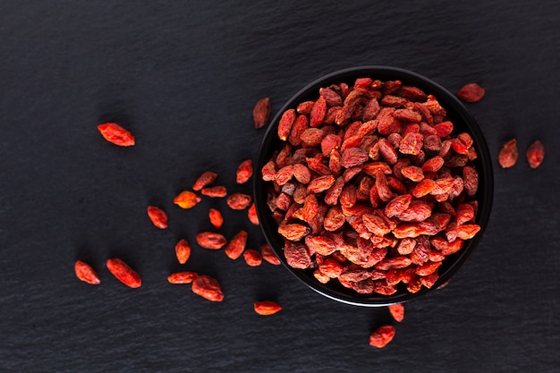 Trockene Goji-Beere des Supergehirnlebensmittels in der schwarzen keramischen Schale auf Schiefersteinbrett