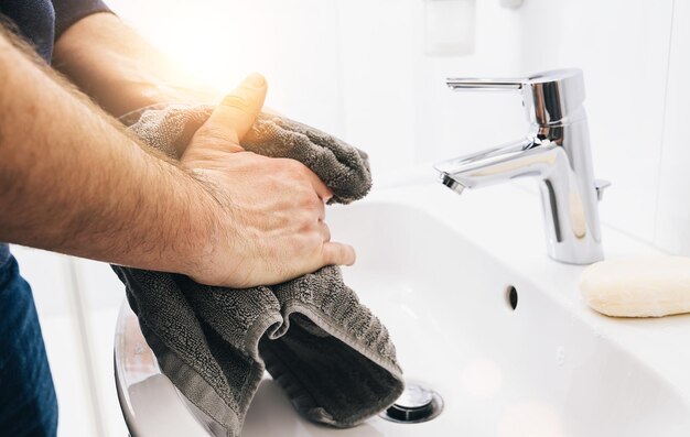 Trockene Hände Mann benutzt Handtuch nach dem Händewaschen am Waschbecken, Coronavirus 2019-ncov Prävention Handhygiene. Schutz vor Corona-Virus-Pandemie durch häufiges Händewaschen.