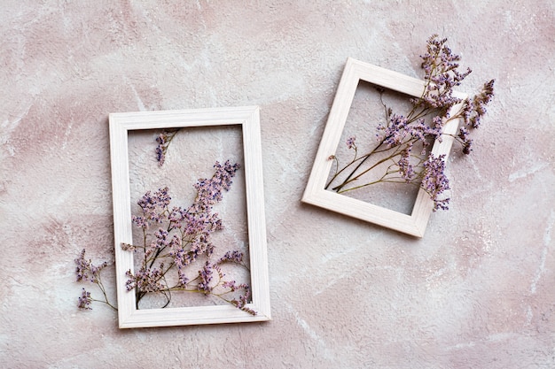 Trockene lila Blumen in zwei weißen Holzrahmen auf einem strukturierten Hintergrund. Romantische Gruß-Vintage-Karte. Ansicht von oben