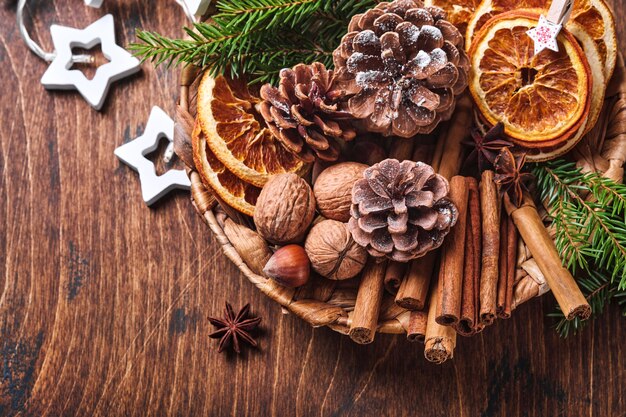 Trockene Orange, Sternanis, Zimt, Tannenzapfen und Tanne in rustikaler Platte auf Holztisch. Hausgemachte Medley-Idee für weihnachtliche Stimmung und Aroma. Umweltfreundliches Weihnachten mit hausgemachten natürlichen Dekorationen.