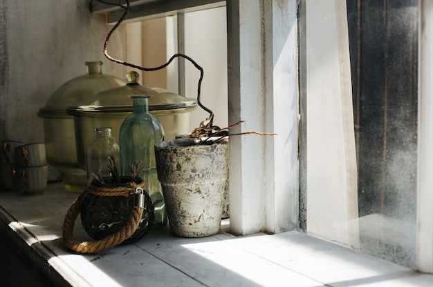 Trockene Pflanze in einer Vase und einem Glasvolumen auf einer Fensterbank in einem großen Holzfenster. Platz für Text