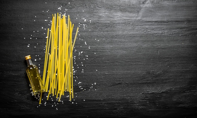 Trockene Spaghetti mit Olivenöl und Salz auf einem schwarzen hölzernen Hintergrund